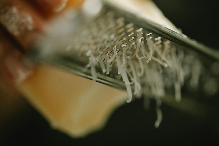 Close-up of cheese being freshly grated on a box grater by hand
