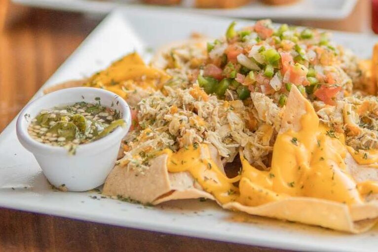 Restaurant-style nachos on a white plate with nacho cheese sauce, shredded chicken, pico de gallo and a jalapeño dipping sauce on the side