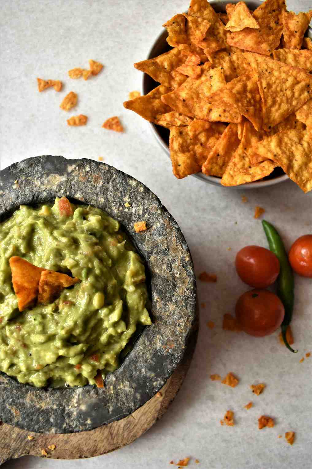 Fresh homemade guacamole in a stone molcajete with tortilla chips, cherry tomatoes and green chilli alongside