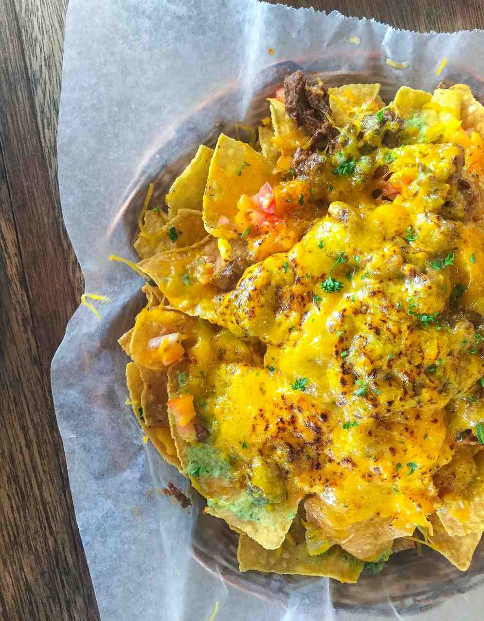 Loaded nachos with melted cheddar cheese, shredded beef, pico de gallo and fresh herbs on parchment paper — inspired by Philly cheesesteak flavours