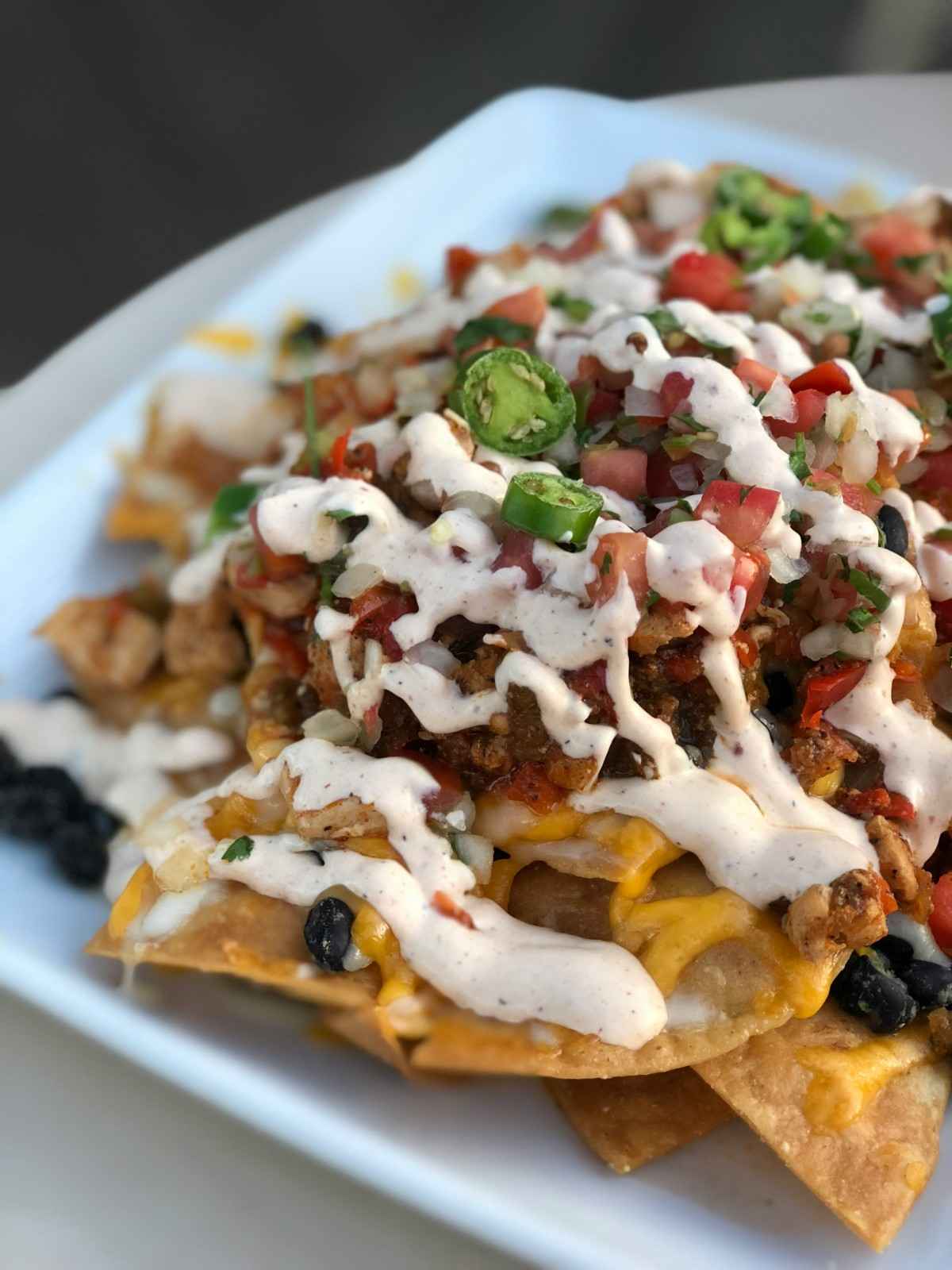 Close up view of plate of nachos with beef, cheese and jalapeño nacho toppings. 