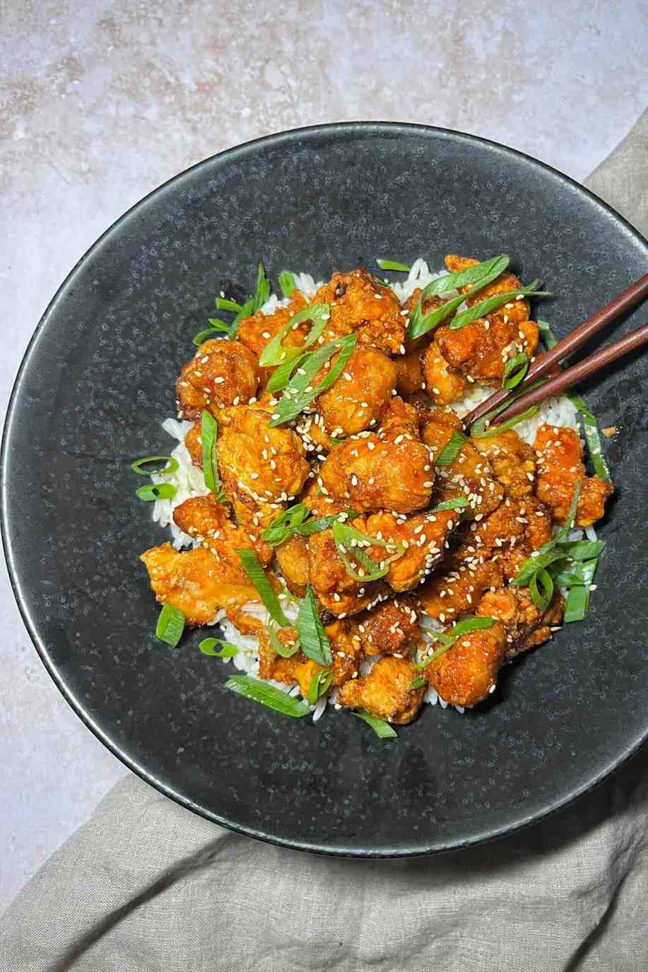 Crispy volcano style chicken bites served over white rice, topped with sesame seeds and sliced green onions.