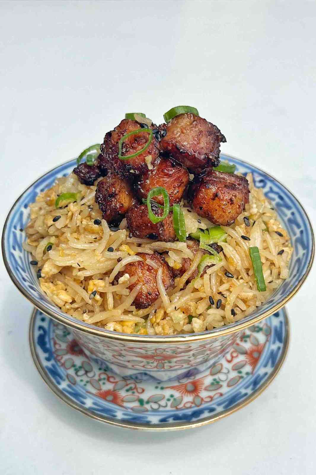 A bowl of egg fried rice topped with caramelized, air-fried pork belly bites and fresh green onions.