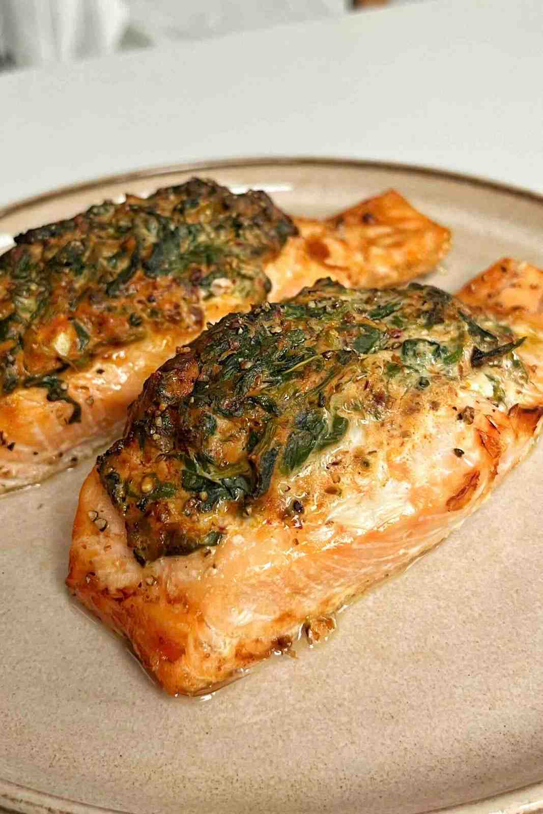 Two air fryer cooked stuffed salmon fillets topped with a thick, golden-brown spinach and herb crust on a neutral plate.