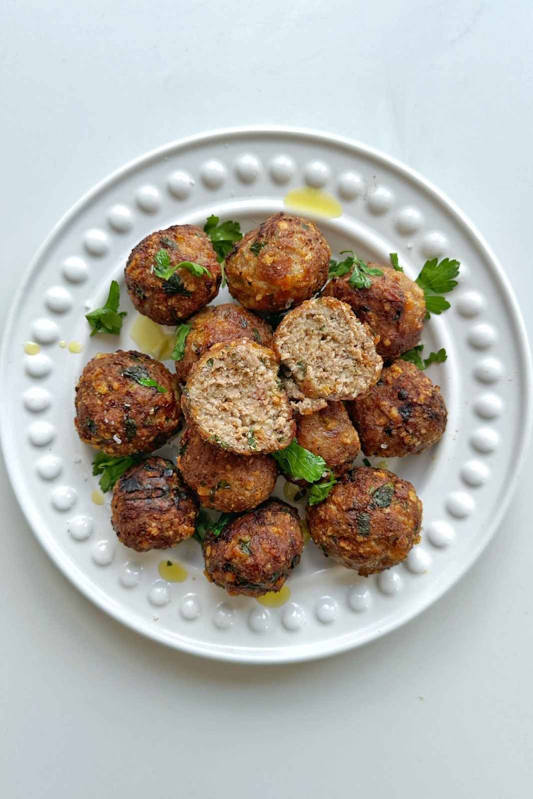 Golden-brown turkey meatballs on a white textured plate, with one broken open to show the juicy interior.