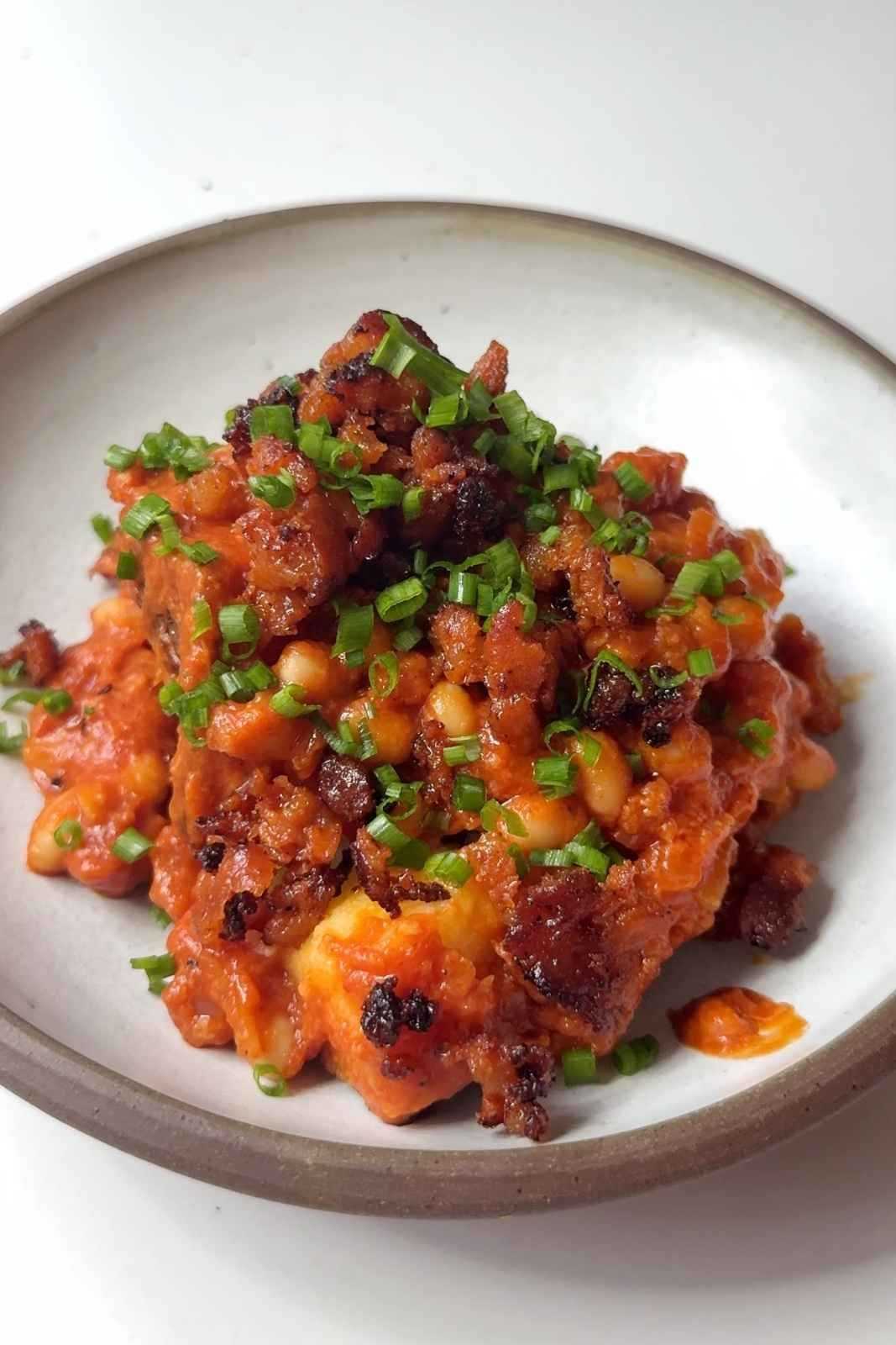 A close-up of a jacket potato topped with smoky baked beans topped and crispy air-fried chorizo and finely chopped chives.