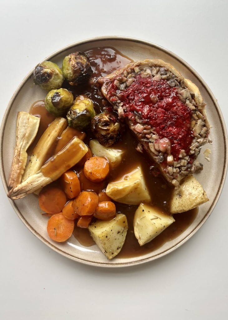 A full roast dinner featuring a savory beet wellington with, roasted potatoes, carrots, parsnips, and Brussels sprouts, served with rich gravy.