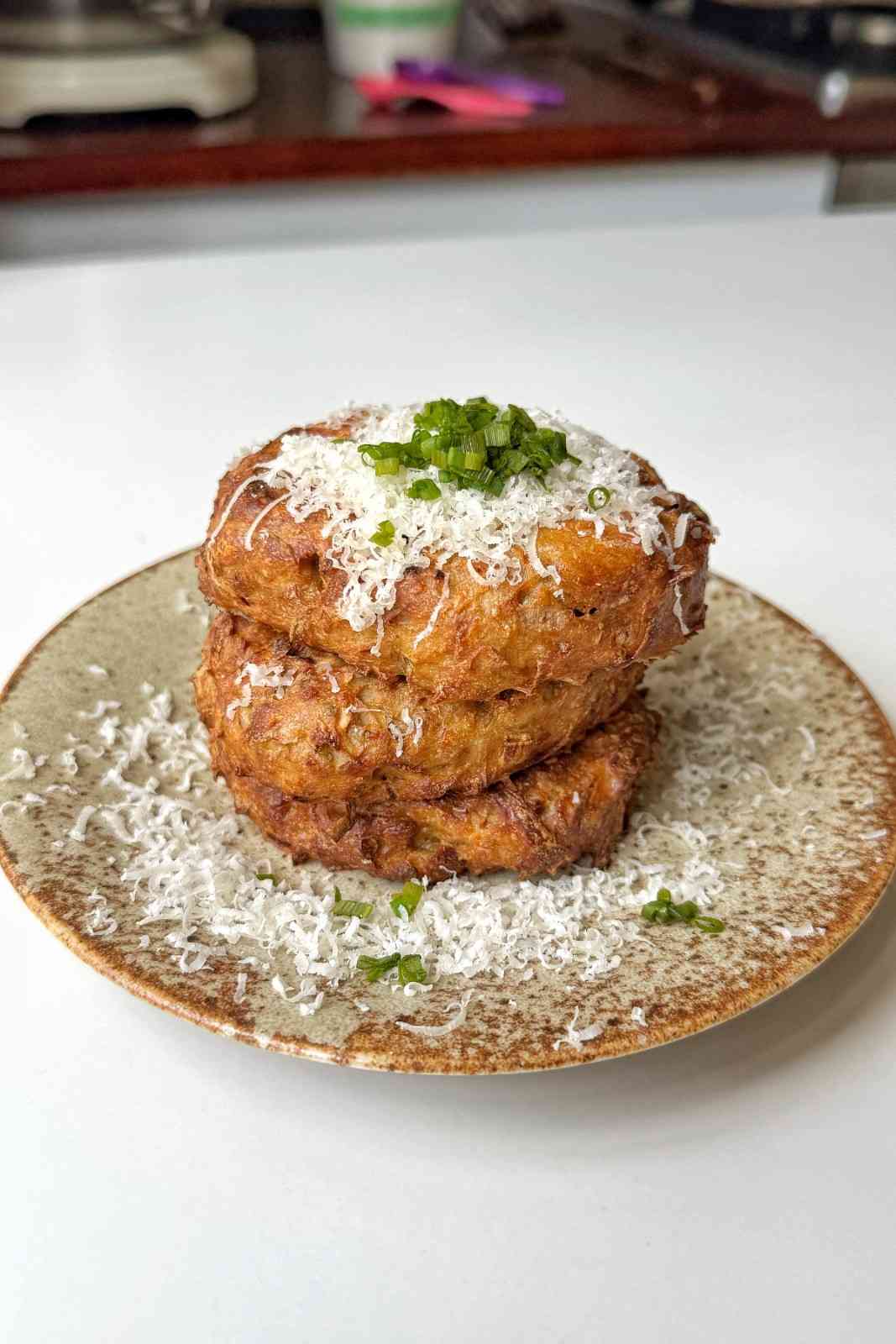 A stack of three golden-brown hash brown patties topped with grated cheese and fresh chives.