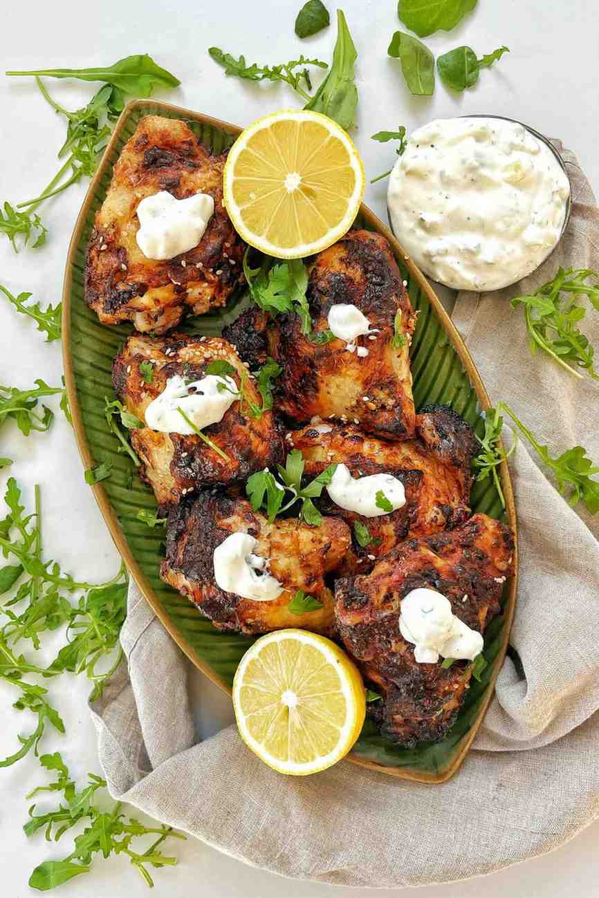 Golden brown air-fryer chicken thighs on a green leaf-shaped platter, topped with yogurt sauce and sesame seeds.