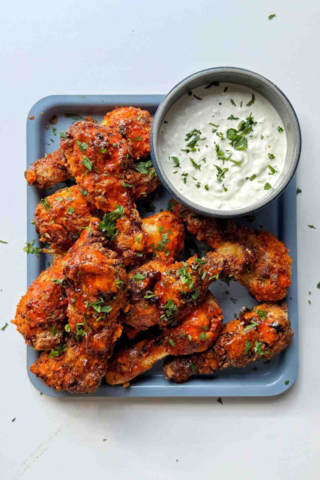 Buffalo chicken drumsticks cooked in an air fryer with a crispy coating, garnished with parsley and served with a blue cheese dipping sauce.