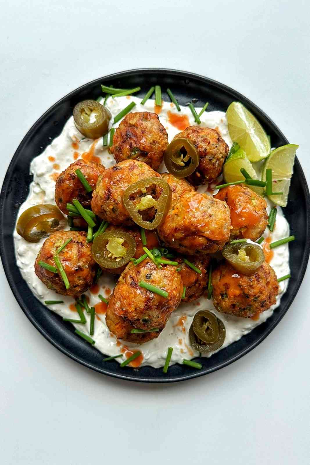 Air-fried chicken meatballs glazed in sauce and served over a creamy base with jalapeños, chives, and lime wedges.