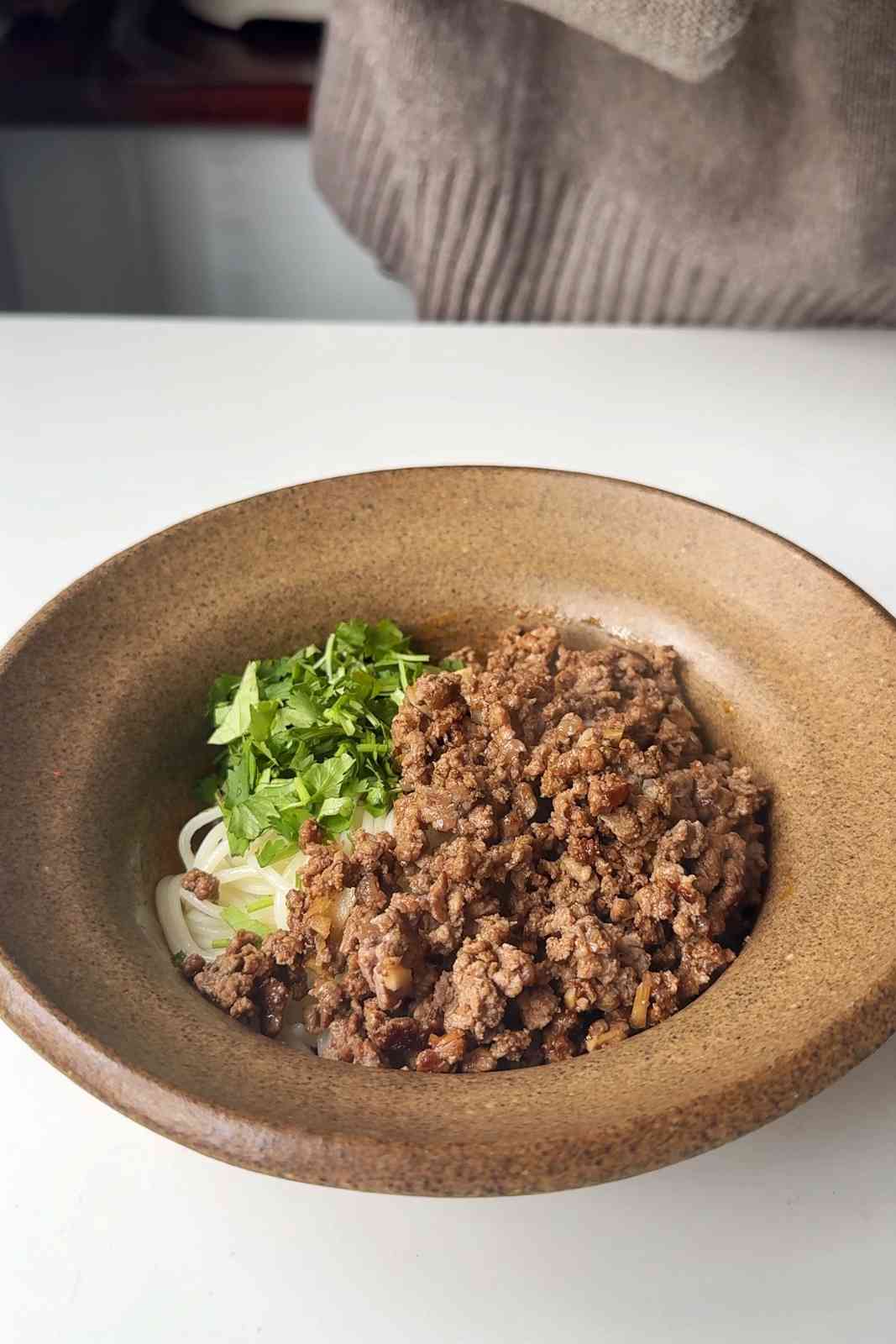 Peanut butter thai noodles topped with fried ground beef and chopped cilantro before mixing together.