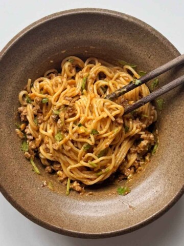 brown bowl with chopsticks filled with Thai-style peanut butter noodles