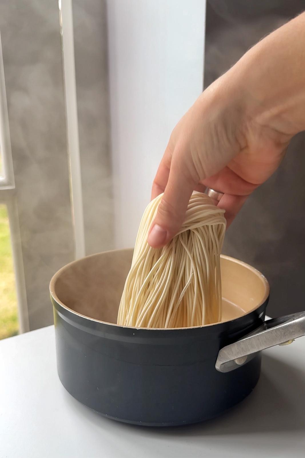 Placing uncooked ramen noodles into a saucepan of boiling water.
