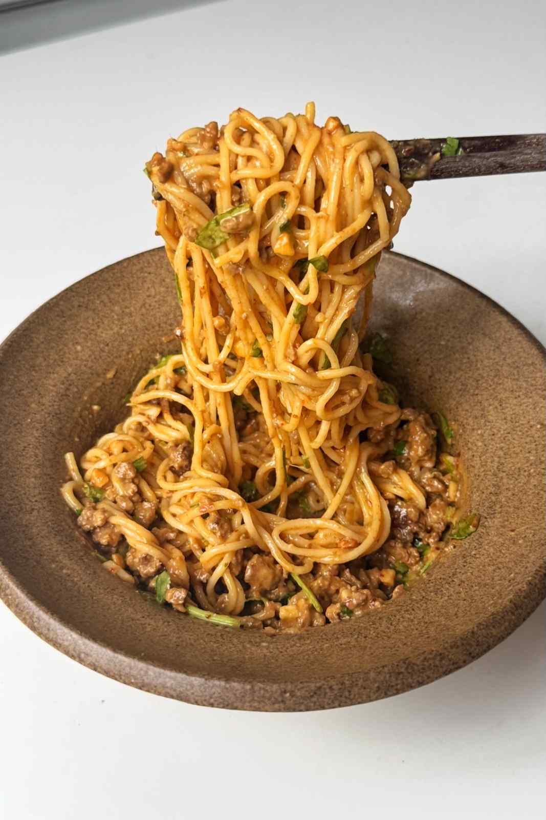 Pulling thai peanut noodles in a brown bowl.