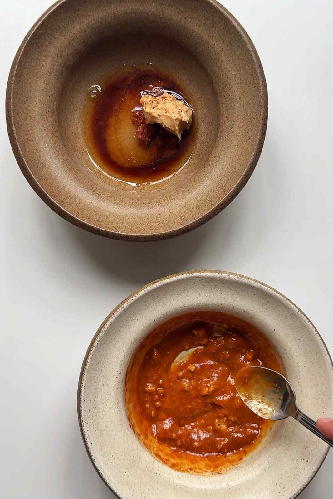 Two bowls with thai peanut butter sauce in the centre with spoon stirring the mixture in one bowl.