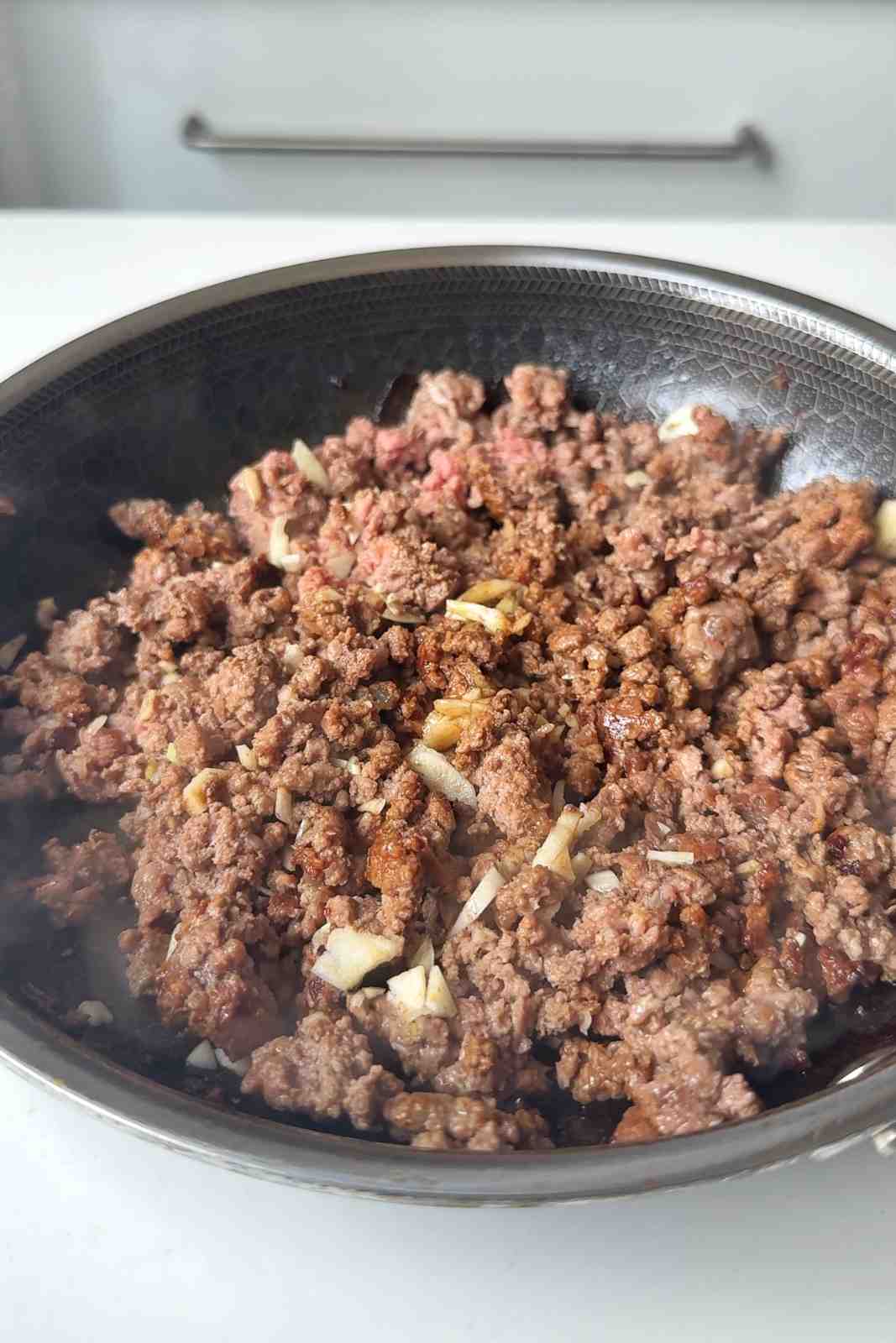 Frying ground beef in a black pan with sliced garlic.