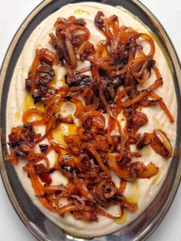White bean dip on silver plater with caramelised onions on top.