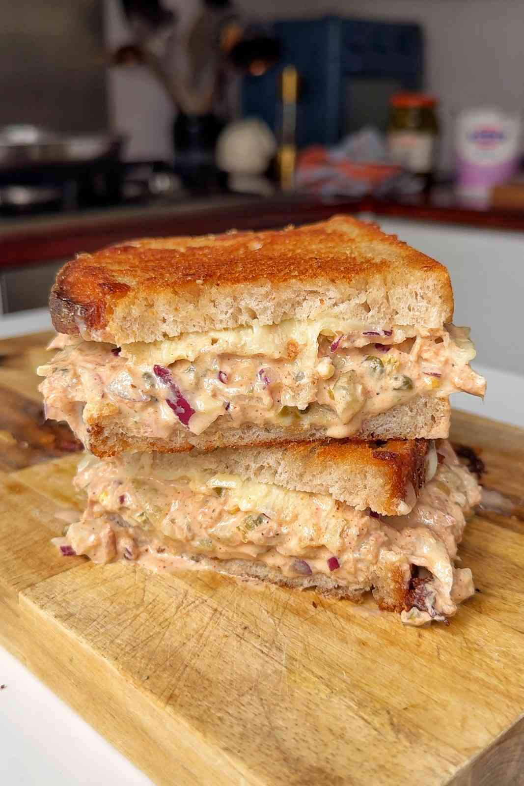 Stacked tuna melt halves with melted cheese and creamy tuna salad with red onion and pickles on golden toasted bread