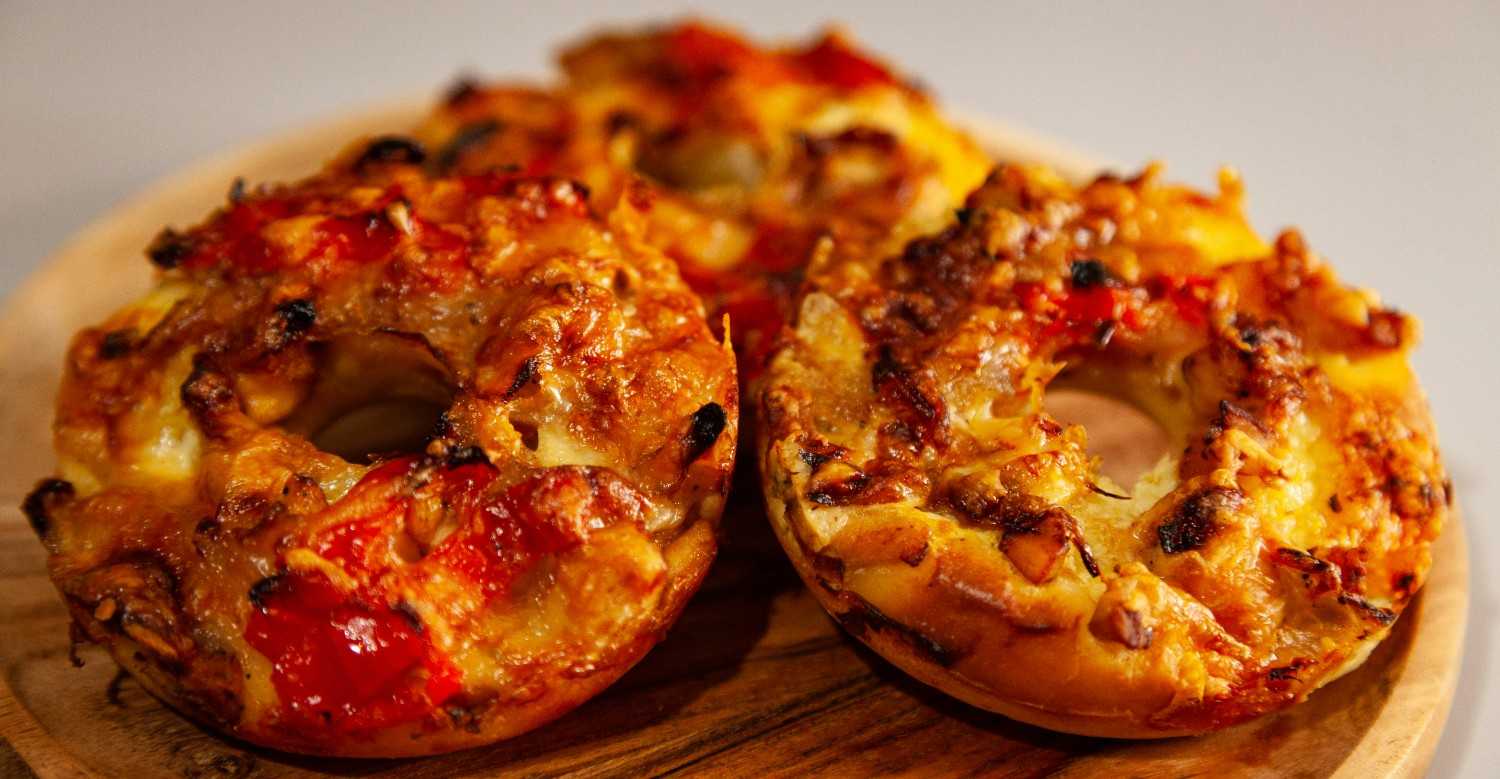 Open-faced pizza bagels topped with melted cheese, marinara sauce, and peppers fresh from the broiler on a wooden board