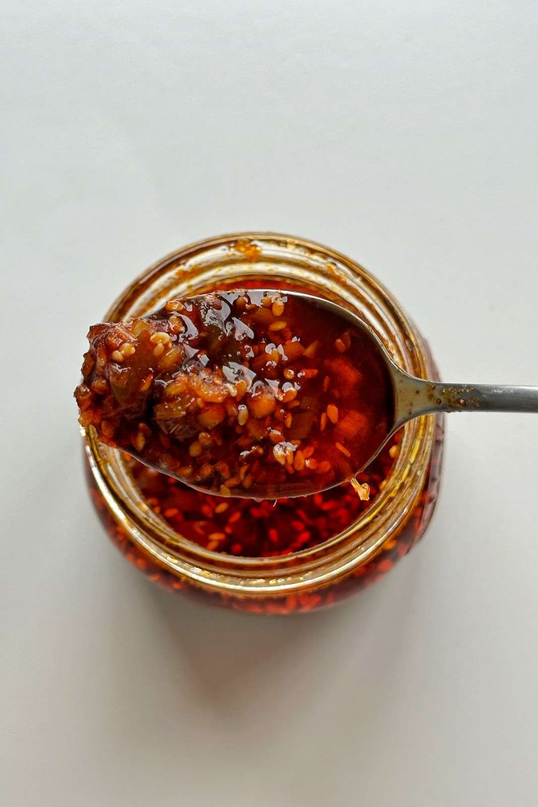 Spoonful of chili crisp with garlic and sesame seeds lifted from an open jar of chili oil