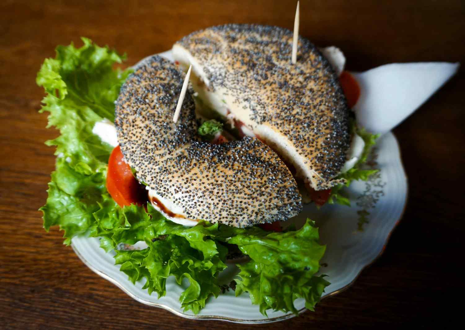 Poppy seed bagel sandwich filled with goat cheese, sliced tomato, and fresh lettuce on a plate