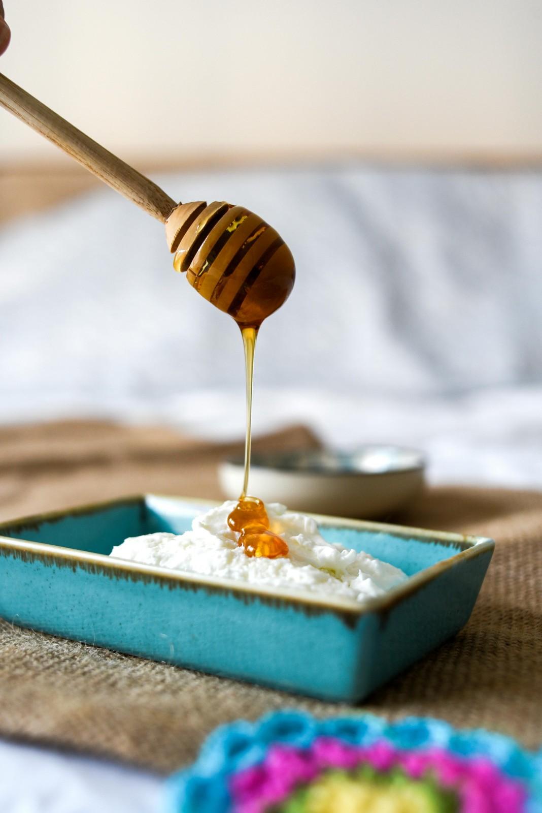 Honey drizzling from a wooden dipper onto a dish of fresh ricotta in a turquoise ceramic bowl
