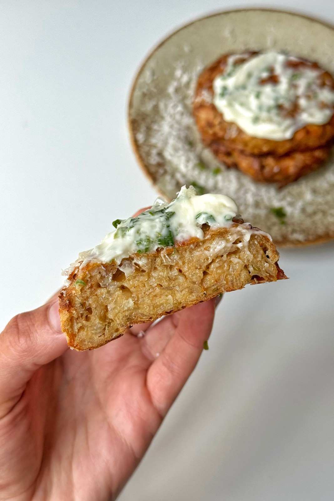 Hand holding a crispy air fryer hash brown topped with a dollop of herbed cream cheese