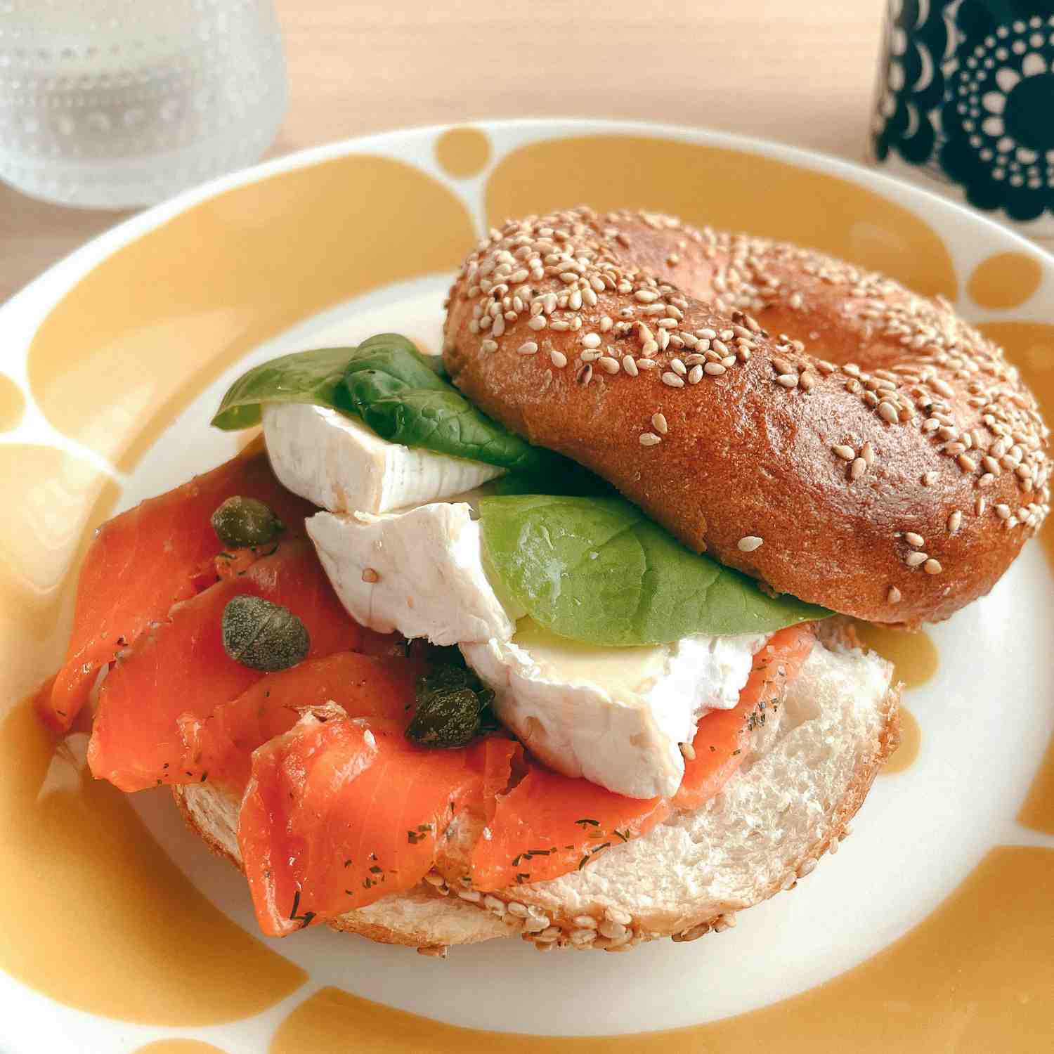 Sesame bagel filled with smoked salmon, sliced Brie, capers, and fresh spinach on a patterned plate