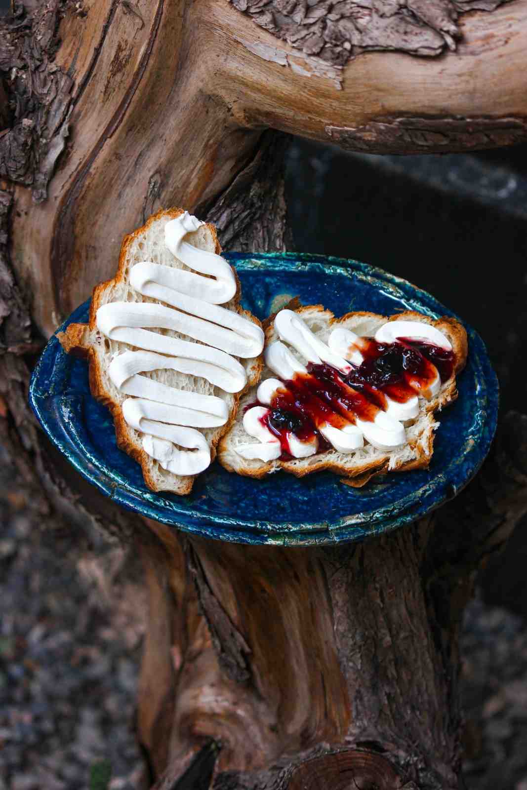 Two slices of croissant with piped cream cheese and berry jam on a blue ceramic plate