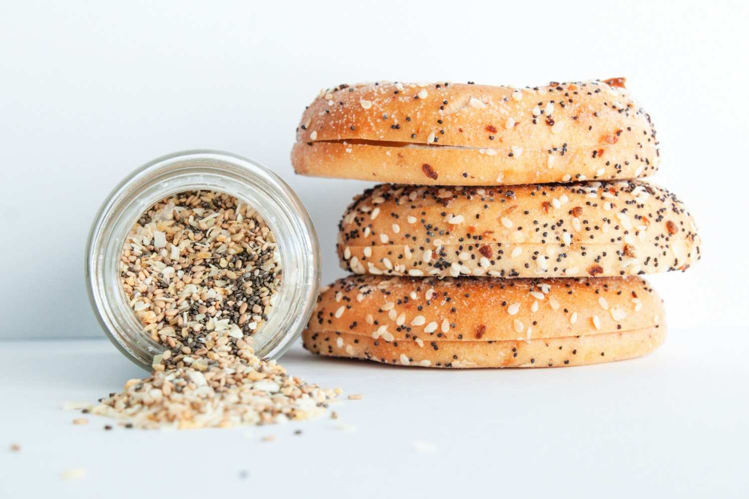 Stack of everything bagels with sesame seeds, poppy seeds, and garlic next to a jar of everything bagel seasoning