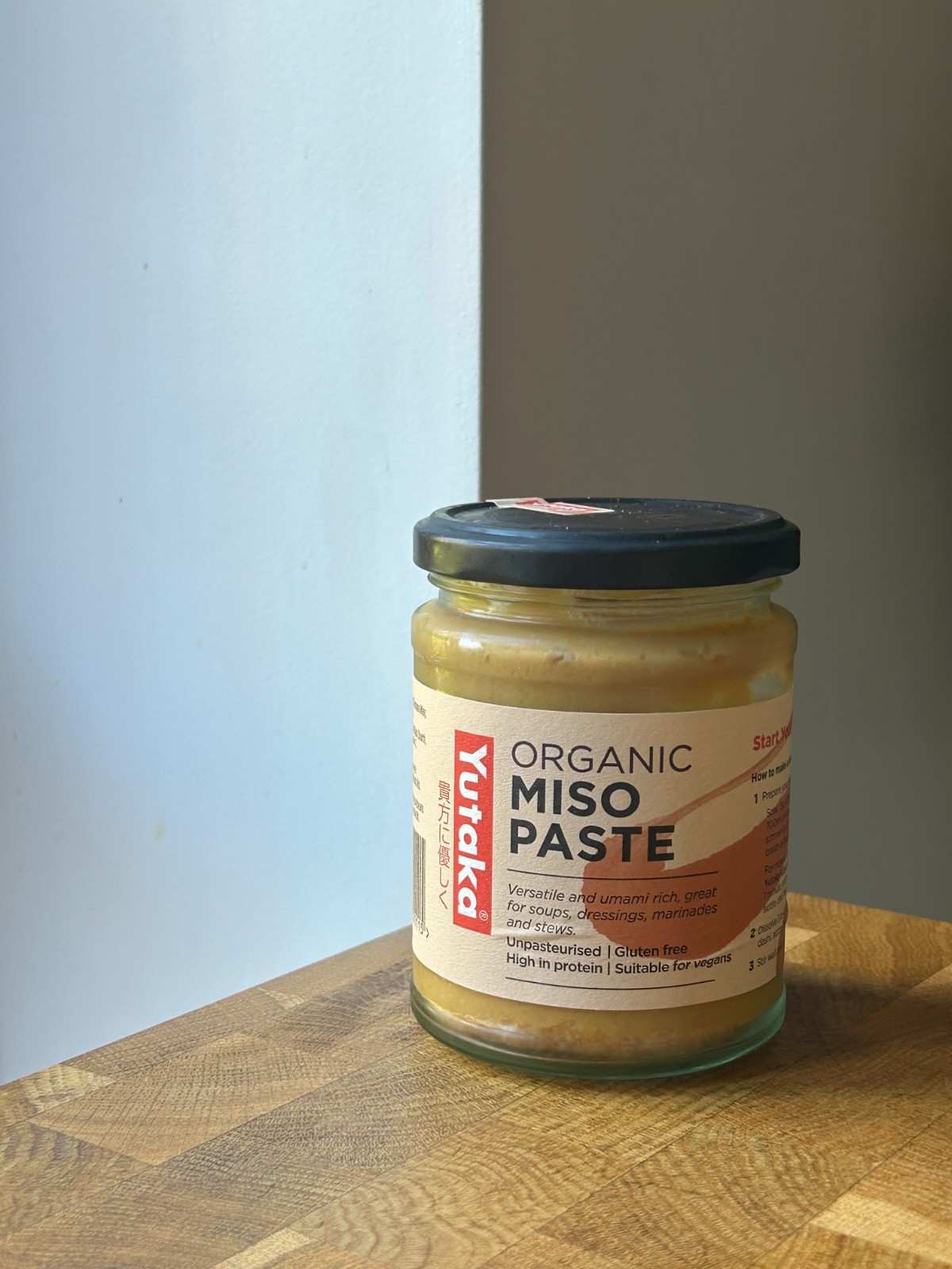 A jar of organic white miso paste on a wooden cutting board.