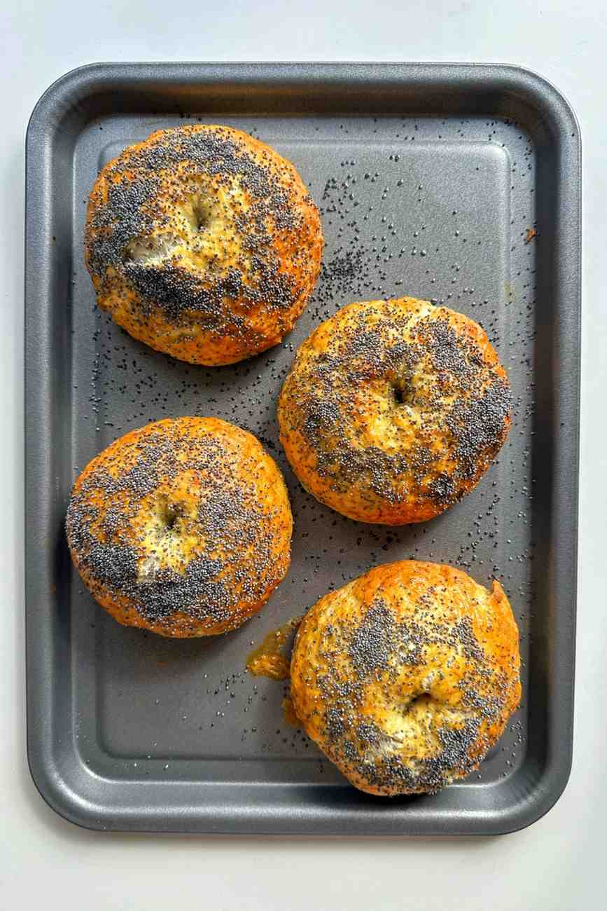 Four golden homemade everything bagels coated in poppy seeds on a baking tray, made with the same everything bagel seasoning that's a fan-favorite baked potato bar topping.