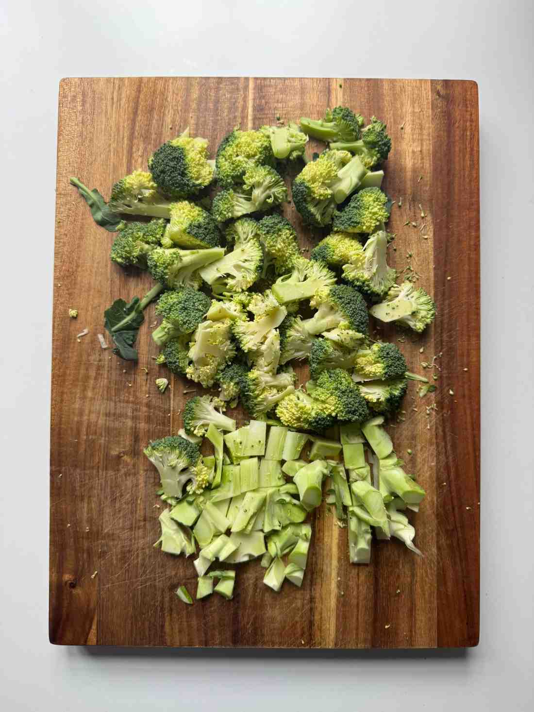 Fresh broccoli florets and chopped stems on a wooden cutting board, ready to be steamed for a classic broccoli and cheese topping.