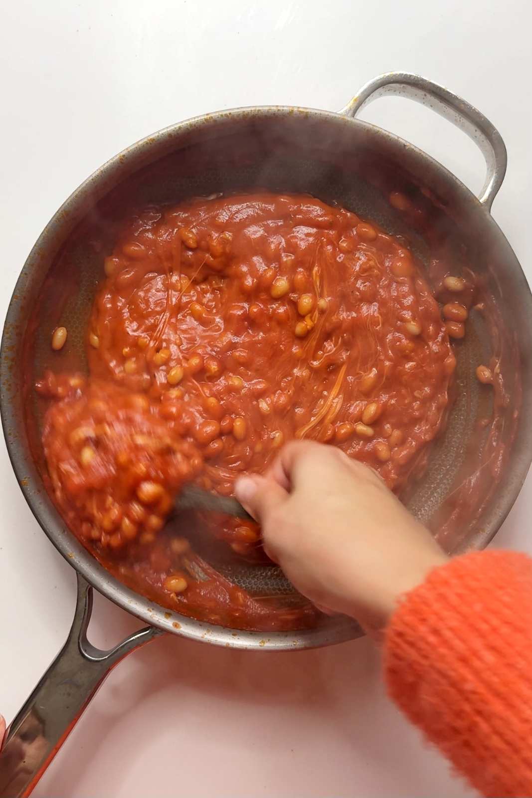 Cheesy baked beans being stirred in a pan with melted cheese creating a stringy, gooey texture, ready to top a baked potato.