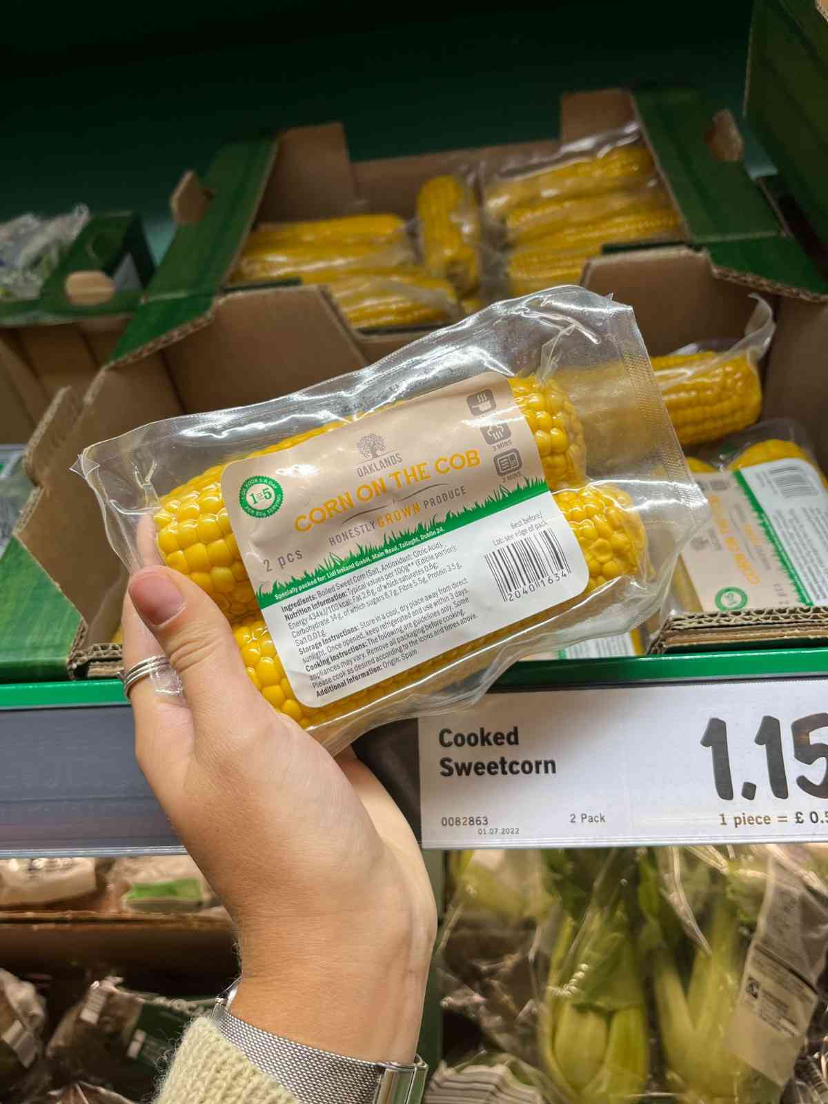 A hand holding a pack of sweet corn on the cob at the grocery store — an easy shortcut for making roasted sweet corn.