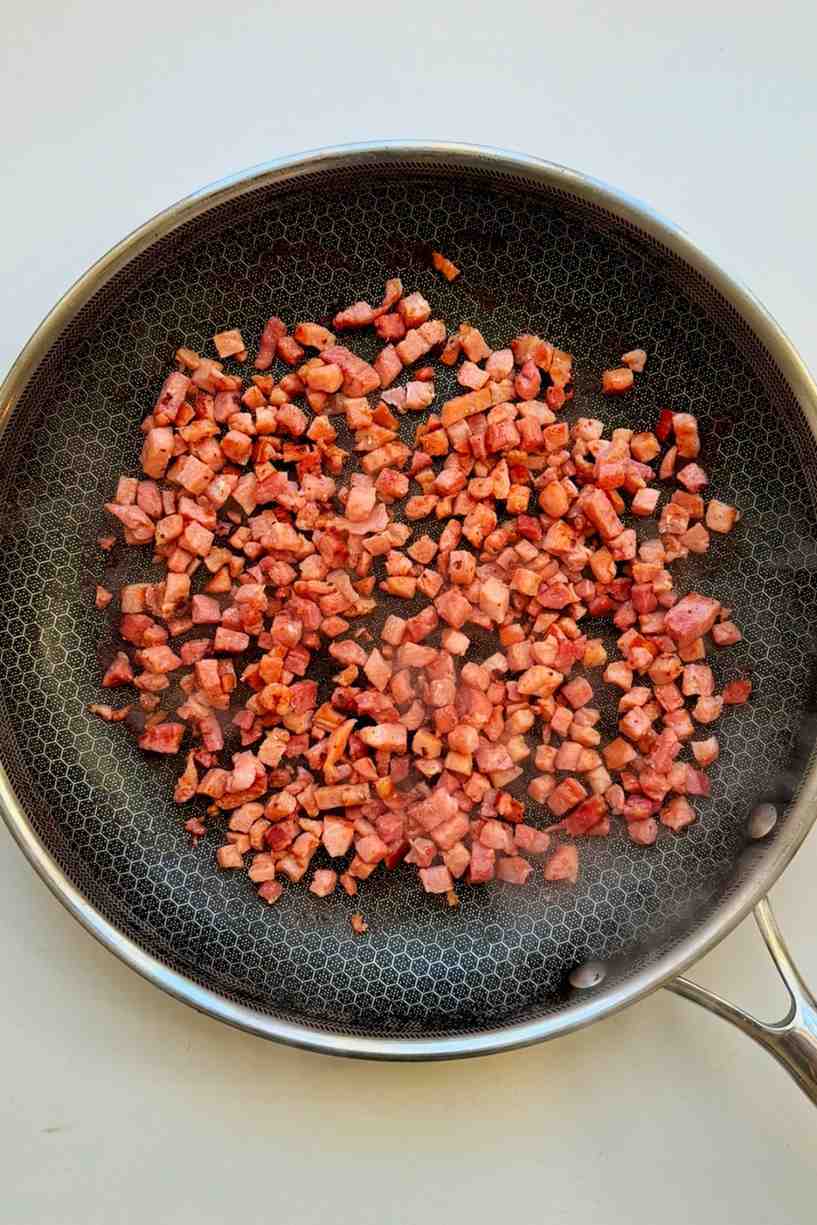 Crispy homemade diced bacon bits fried until golden in a stainless steel skillet, ready to serve as a baked potato bar topping.