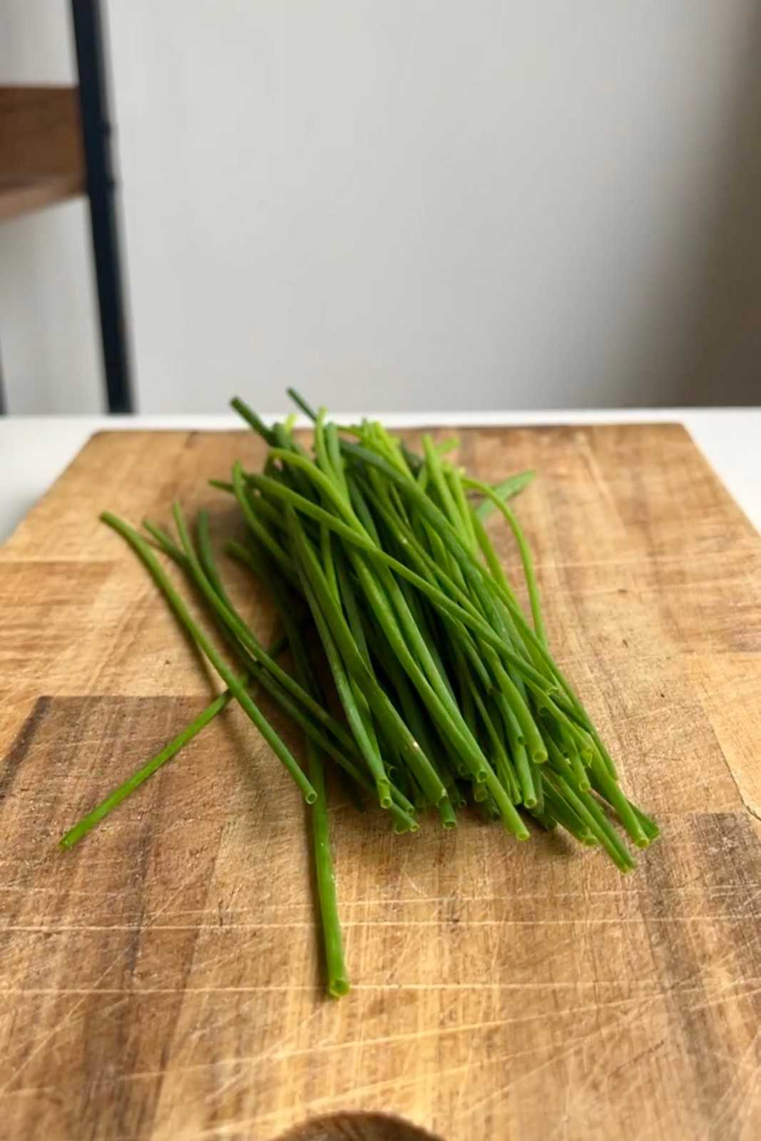 A bunch of fresh chives on a wooden cutting board, ready to be finely chopped as a fresh, vibrant baked potato bar topping.
