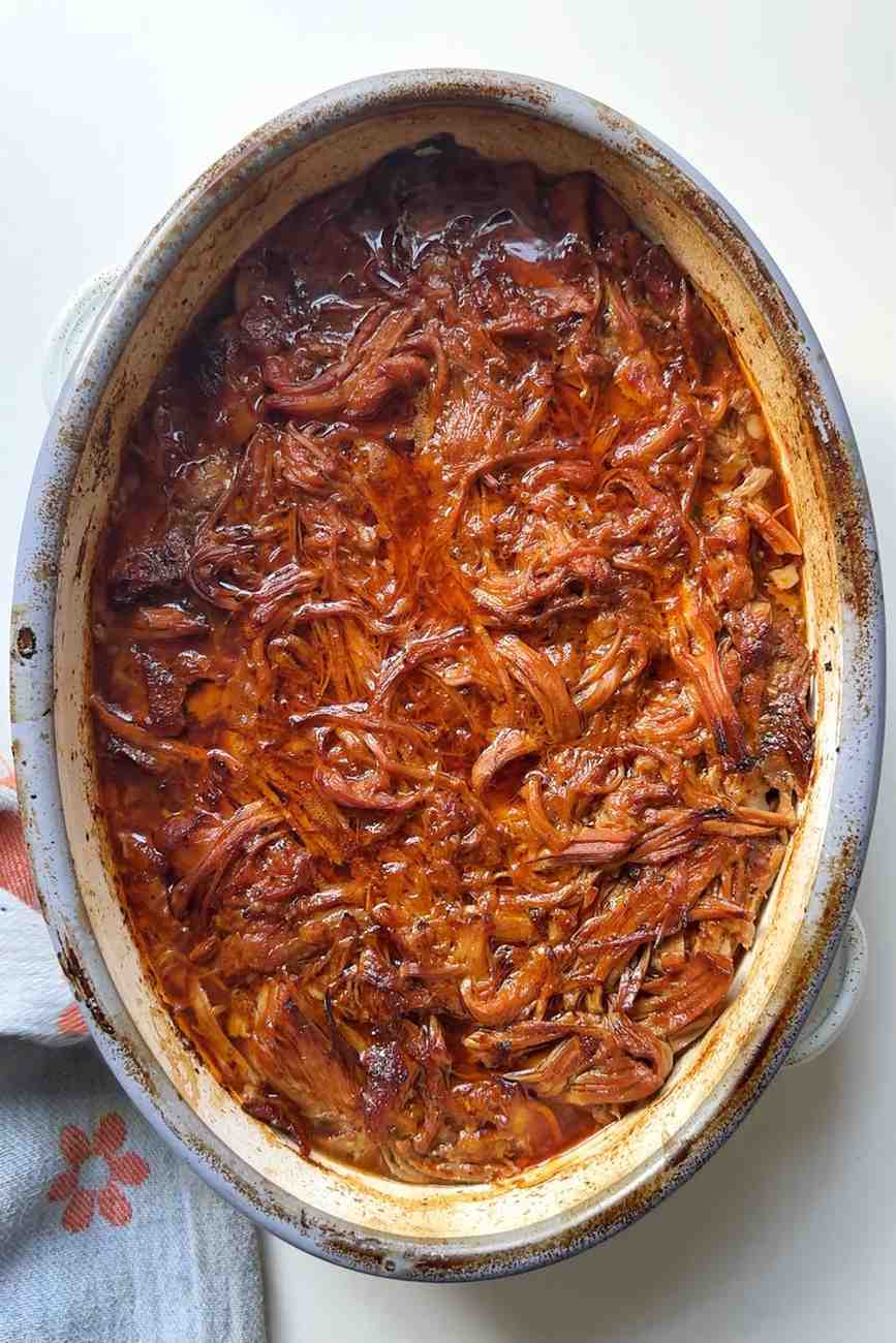 Slow-cooked BBQ pulled pork in a rich, glossy sauce served in an oval ceramic dish, ready to use as a baked potato bar topping.