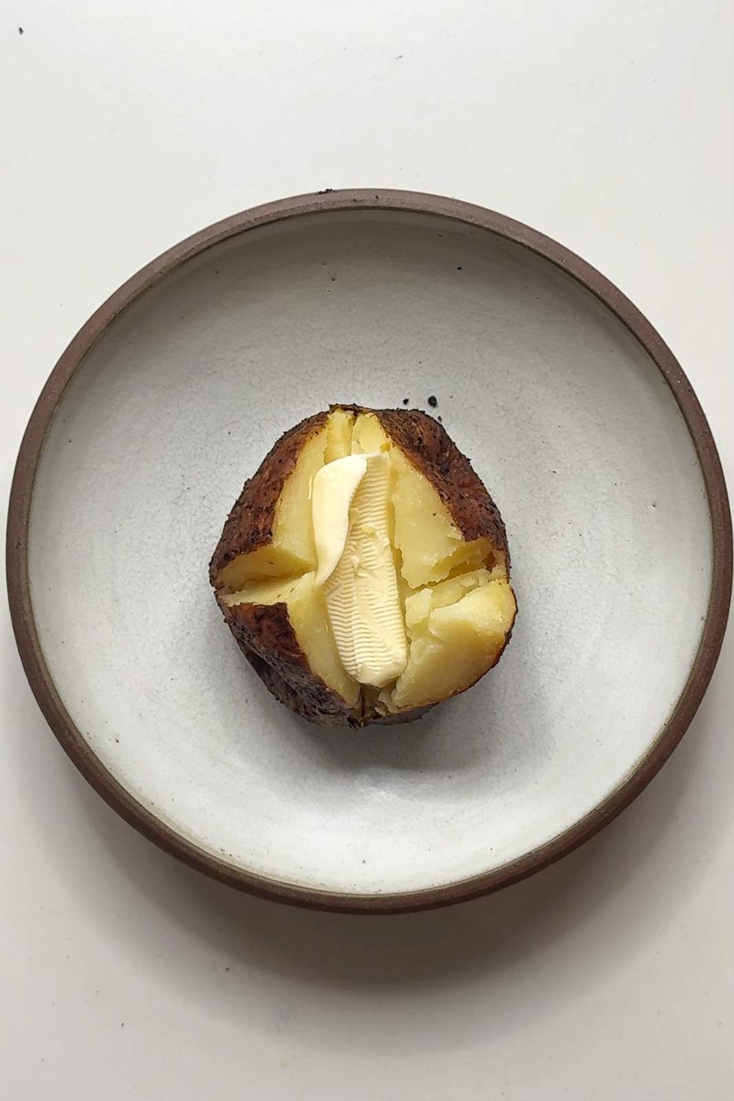 A crispy-skinned baked potato split open with a generous pat of real butter melting into the fluffy flesh, served on a ceramic plate.