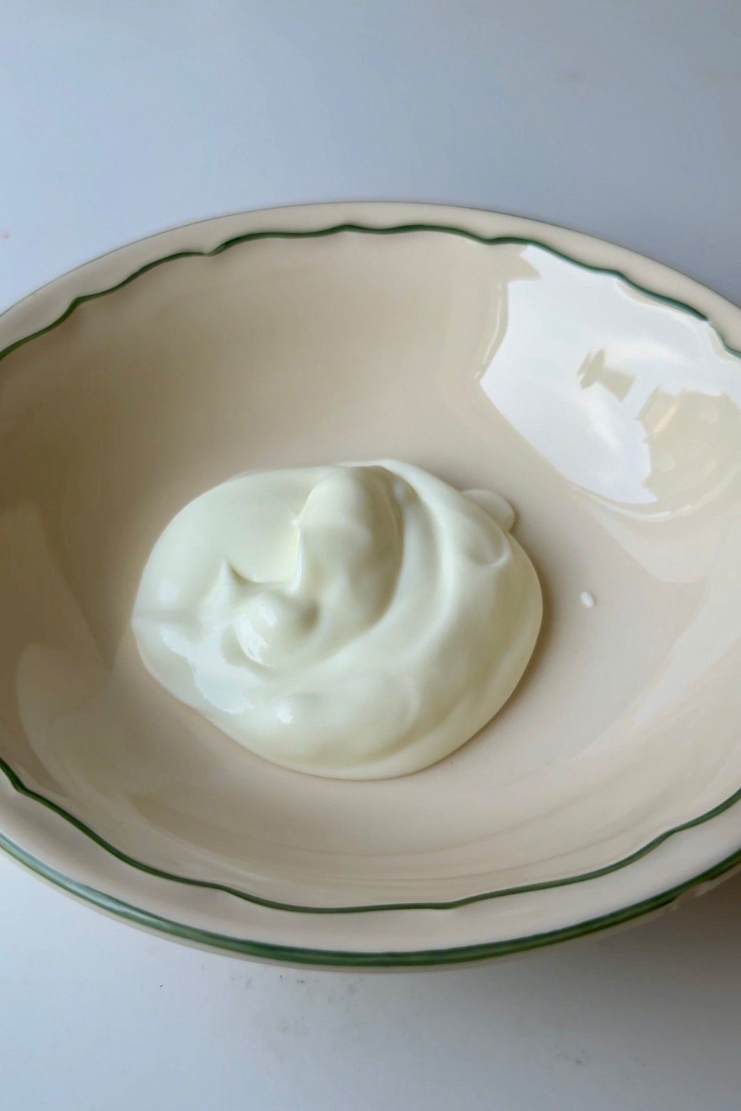 A dollop of thick, creamy sour cream in a green-rimmed ceramic bowl, an essential topping for any loaded baked potato bar.