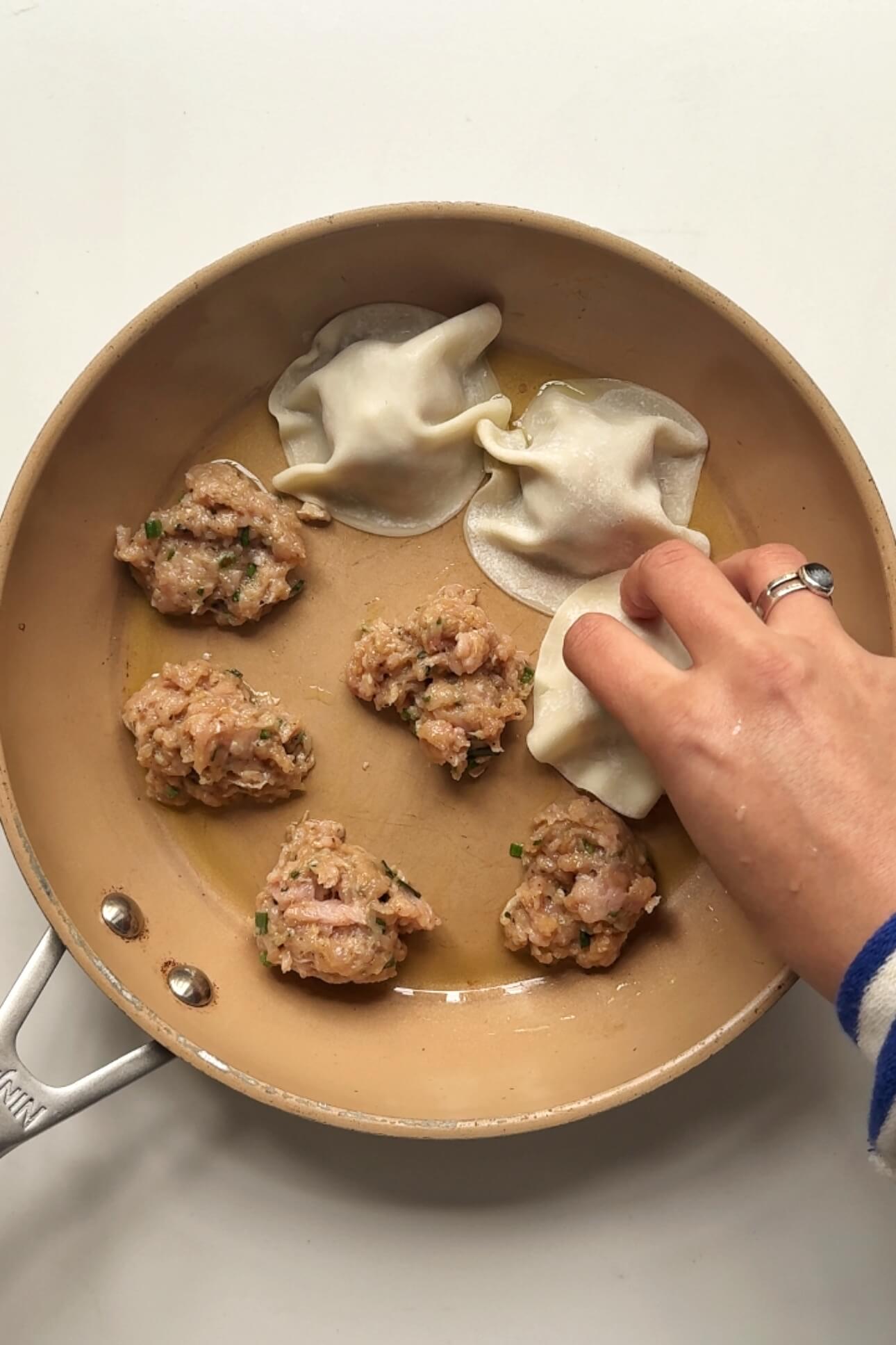 Placing dumpling wrappers on top of dumpling filling in a pan.