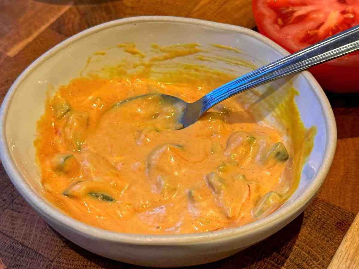 A small bowl of burger sauce with pickle chunks within.
