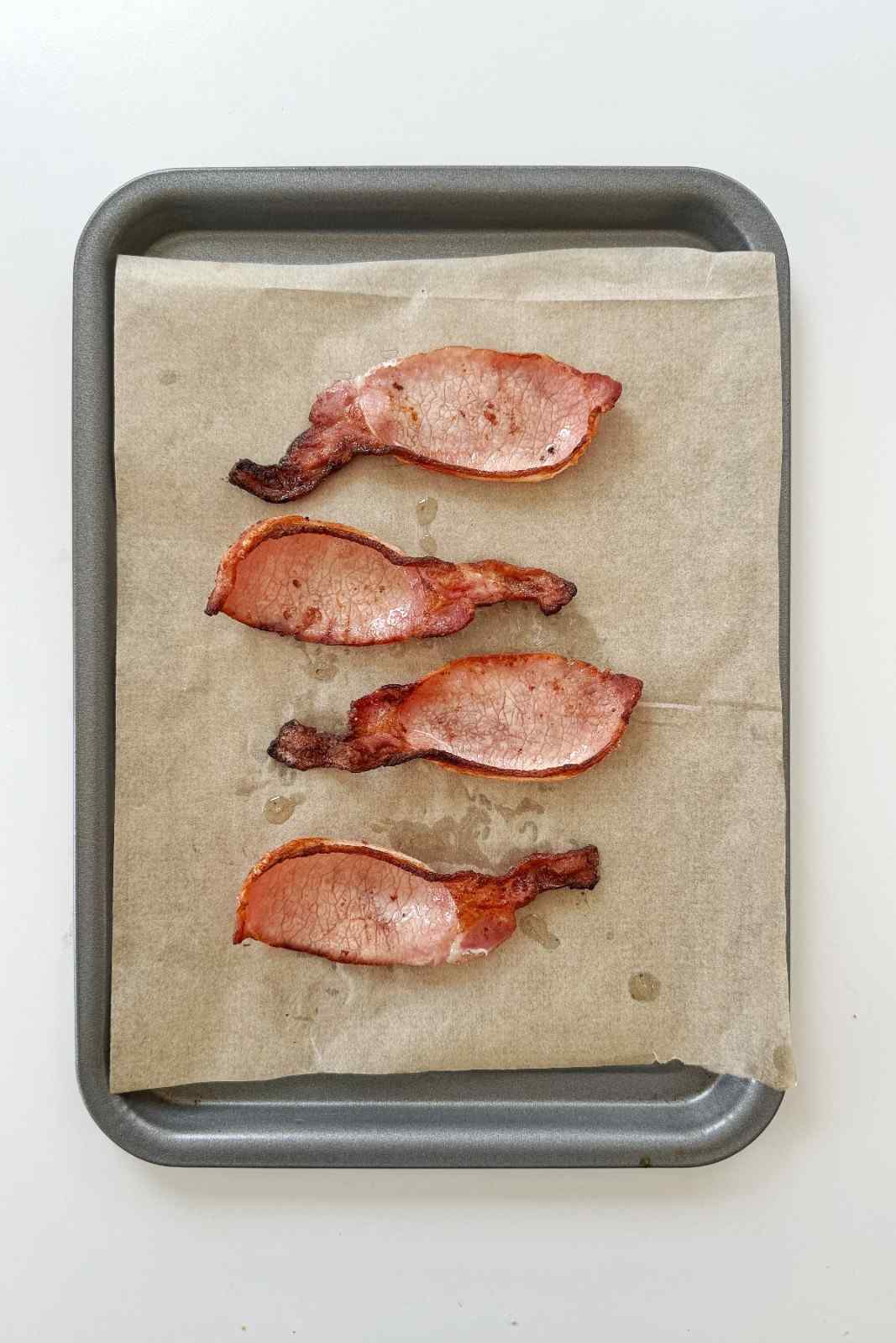 Four strips of crispy oven-baked bacon on a parchment-lined baking tray.