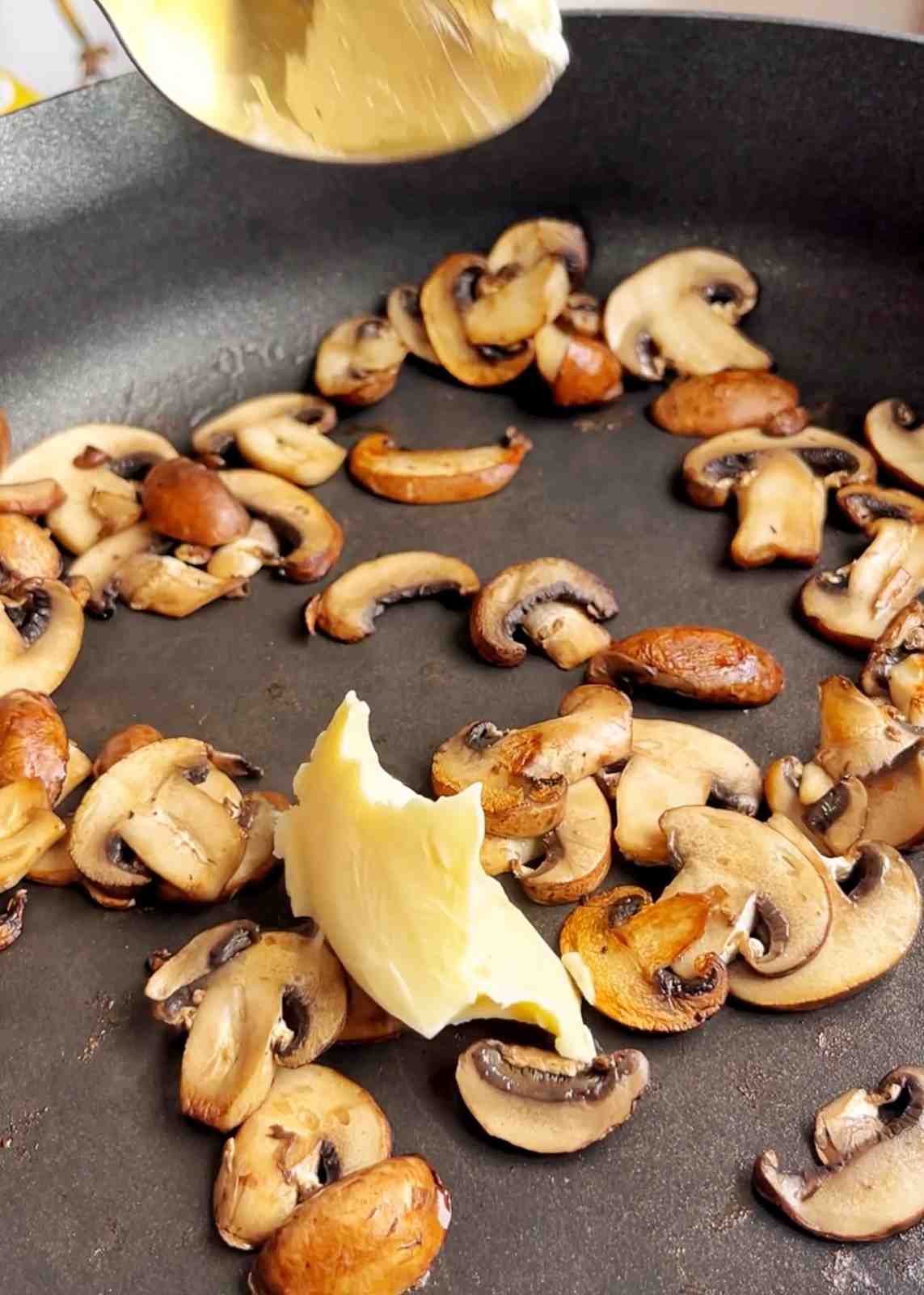 Sliced chestnut mushrooms being sautéed in butter in a black non-stick pan until golden brown.