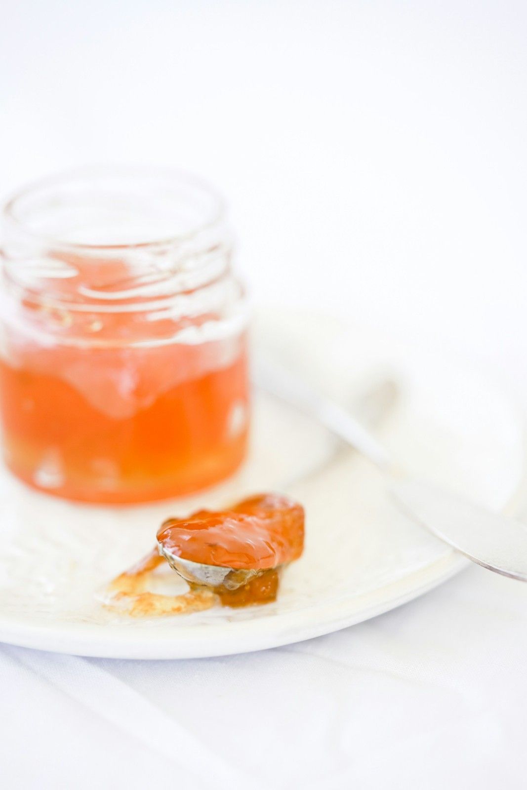 A small glass jar of homemade hot pepper jelly with a spoonful resting on a white plate.