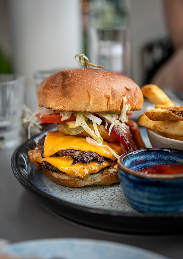 A stacked double cheeseburger with two slices of melted American cheese oozing over the edges of the beef patties, served with thick-cut fries and ketchup.