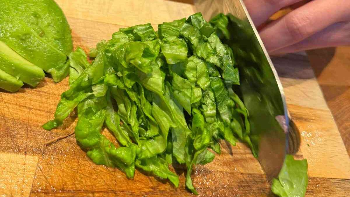 Finely shredded iceberg lettuce being chopped on a wooden chopping board, ready to be used as a burger topping.