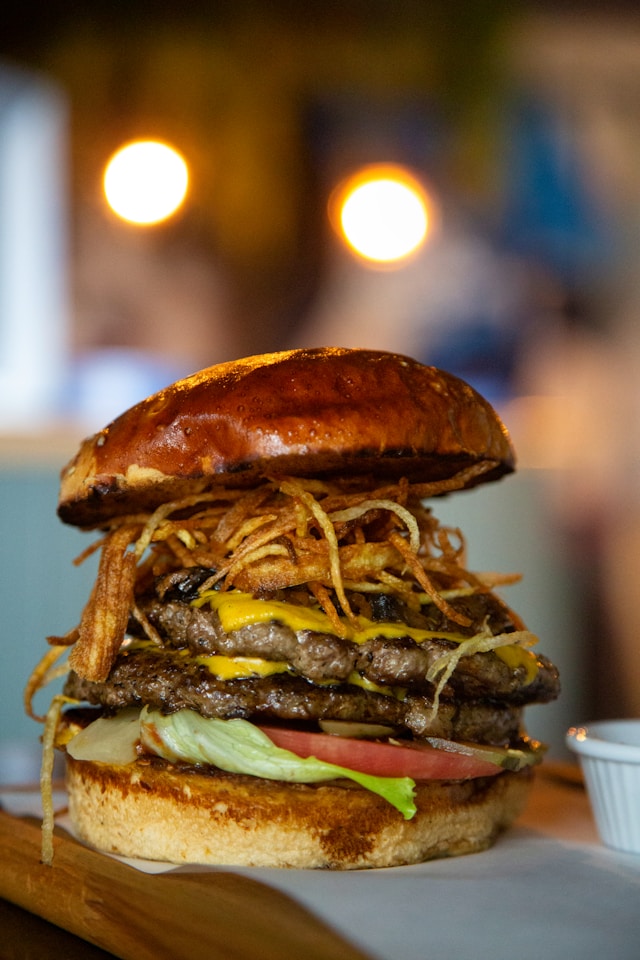 A double smash burger stacked high with melted American cheese, pickles, tomato, and a towering pile of thin shoestring fries piled on top.