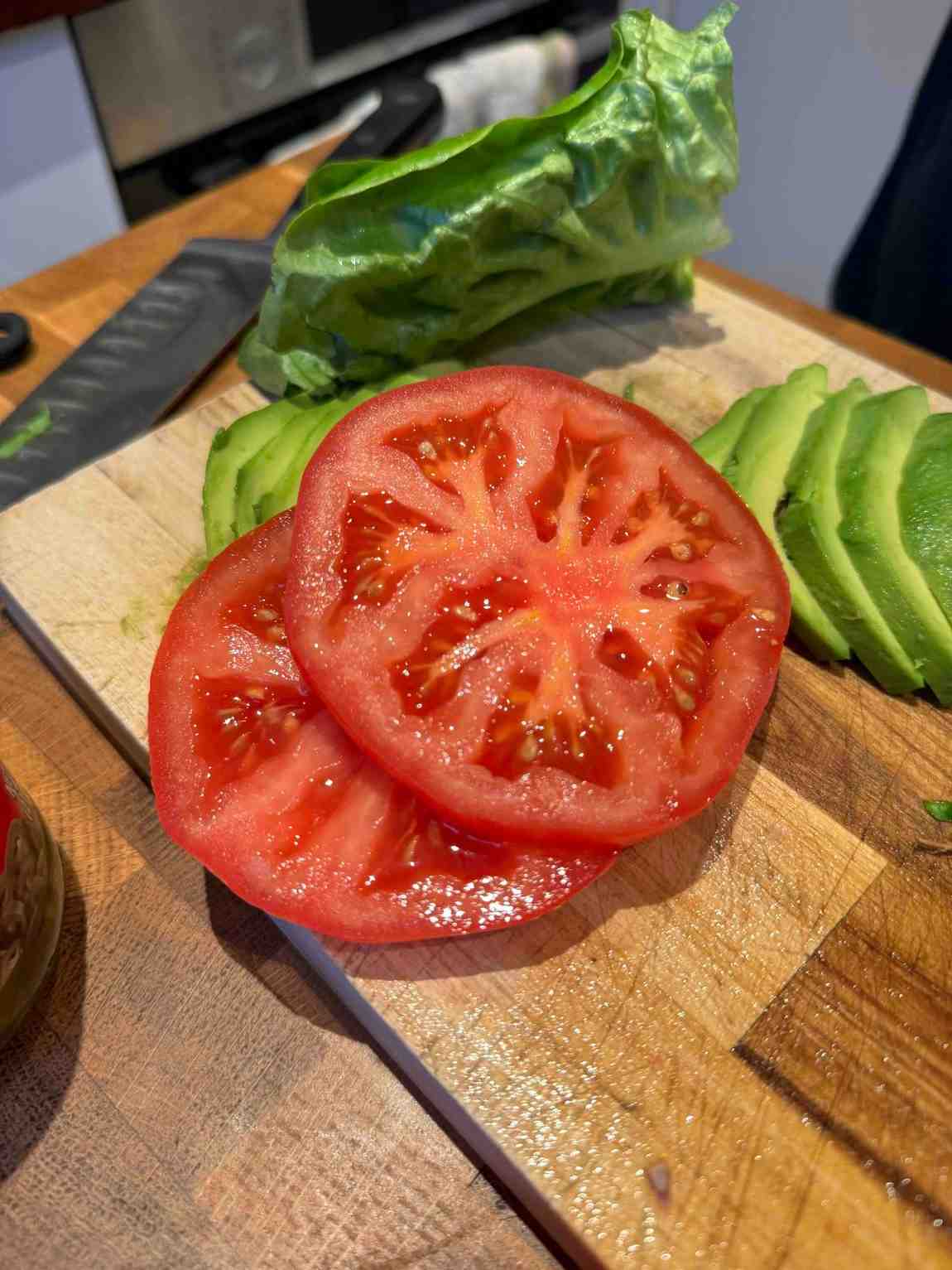 Two slices of beefsteak tomato on a wooden chopping board ready to be used on top of a burger.